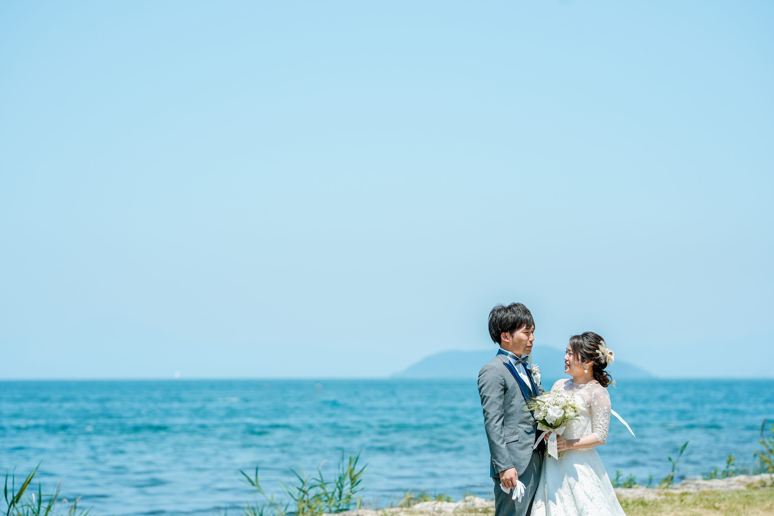 琵琶湖を背景に洋装で立つ新郎新婦｜滋賀フォトウェディング 前撮り